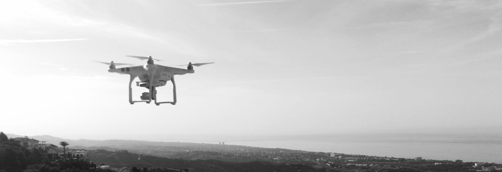 Drone DJI Phantom volando sobre colinas con vista al mar en blanco y negro.